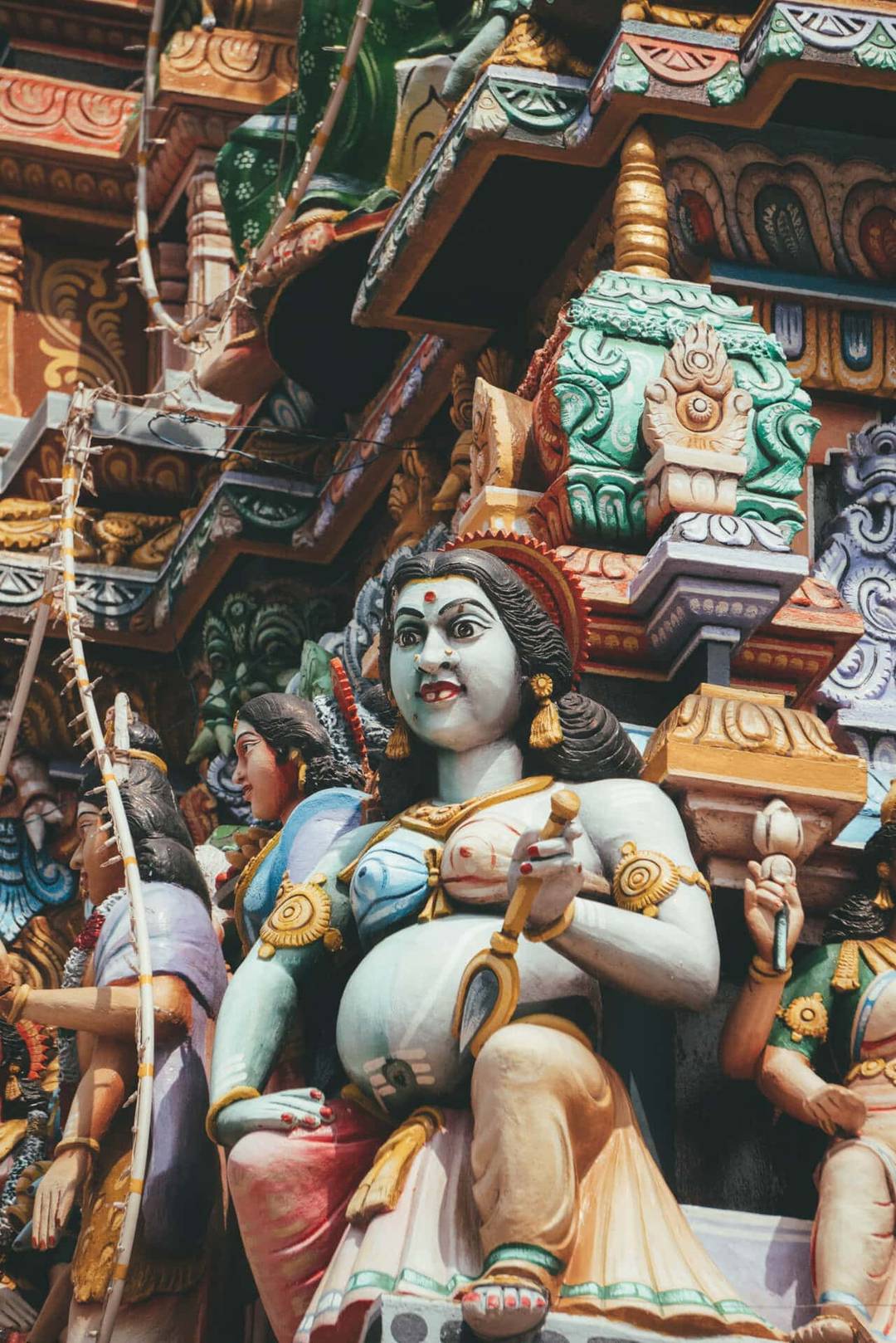 Colorful sculpted figures of Hindu deities and mythological characters adorn the ornate facade of Sri Pathrakali Amman Kovil, featuring intricate details and vibrant patterns.