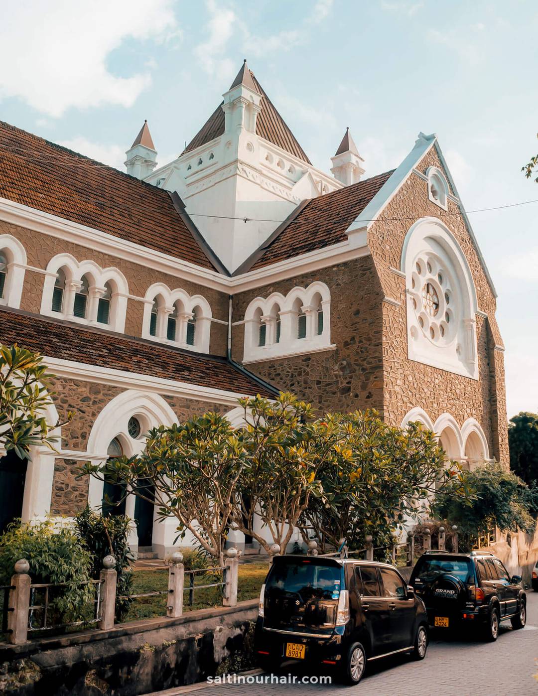 Exterior of Groote Kerk church in Galle, Sri Lanka, with stone walls, white arched windows, and cars parked outside.