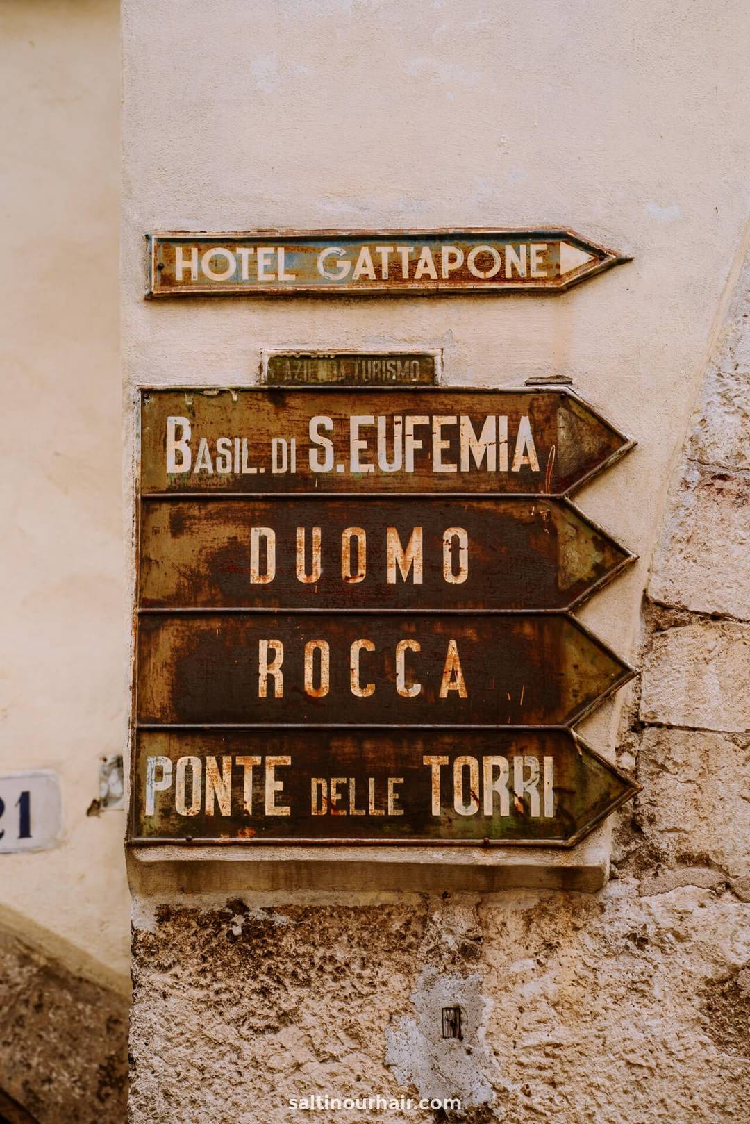 Weathered directional signs on a stone wall point toward Hotel Gattapone, Basil di S. Eufemia, Duomo, Rocca, and Ponte delle Torri&mdash;highlighting classic things to do in Umbria.