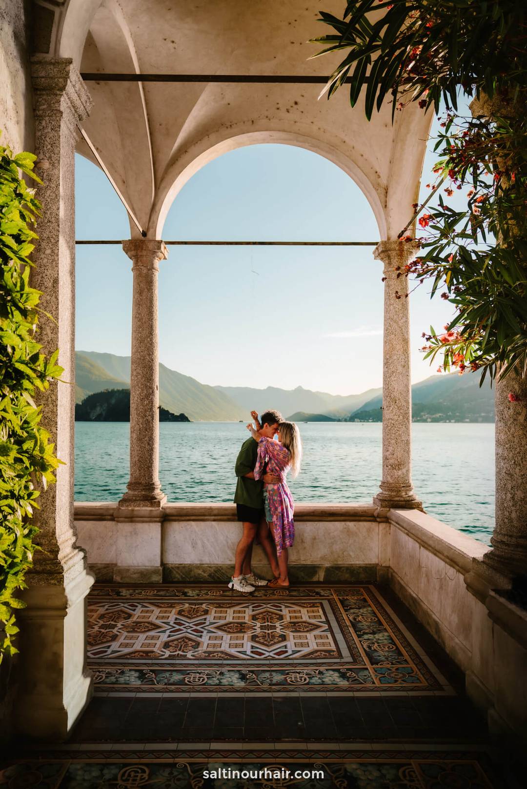couple hugging under the authentic arches of villa monastero surounded by the water of lake como italy