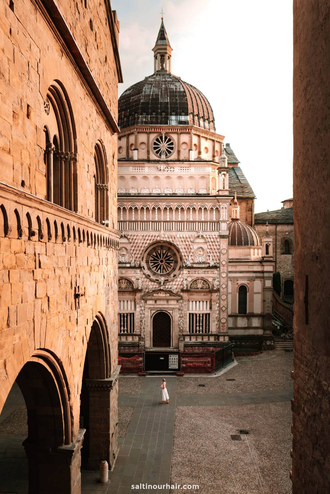 A person stands in front of the ornate Colleoni Chapel, a Renaissance-style building with a large dome, in an old European city square at sunset&mdash;an unforgettable stop on any italy itinerary 2 weeks long.