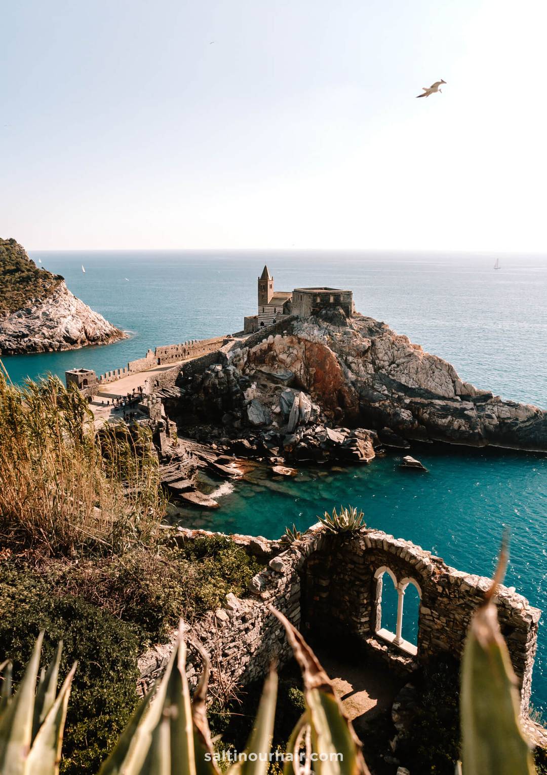 Stone church on a rocky promontory overlooking blue sea, with ruins and greenery in the foreground&mdash;a highlight to explore on your Italy 7 day itinerary as a bird soars overhead.