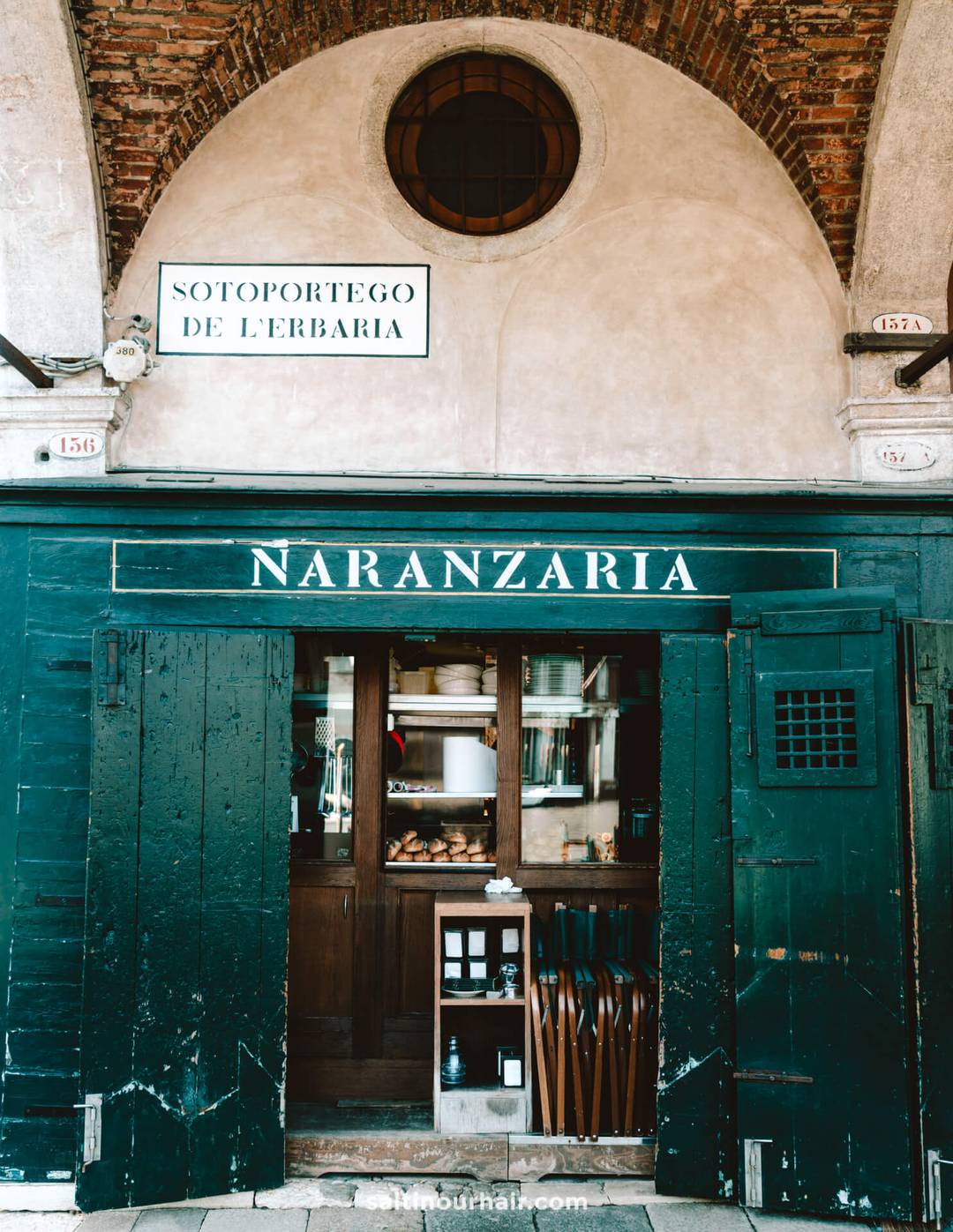 Green storefront of NARANZARIA with open wooden doors, shelves with bottles and dishes inside, and arched stonework above the entrance&mdash;a charming spot to discover on your Italy 7 day itinerary.