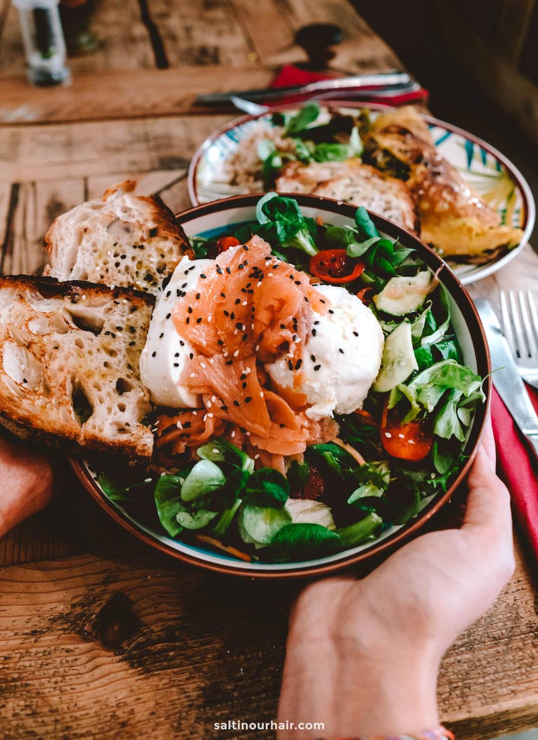 A bowl of salad with smoked salmon, burrata cheese, cherry tomatoes, cucumbers, greens, and two slices of toasted bread on a wooden table&mdash;perfect inspiration for your Italy 7 day itinerary food adventures.