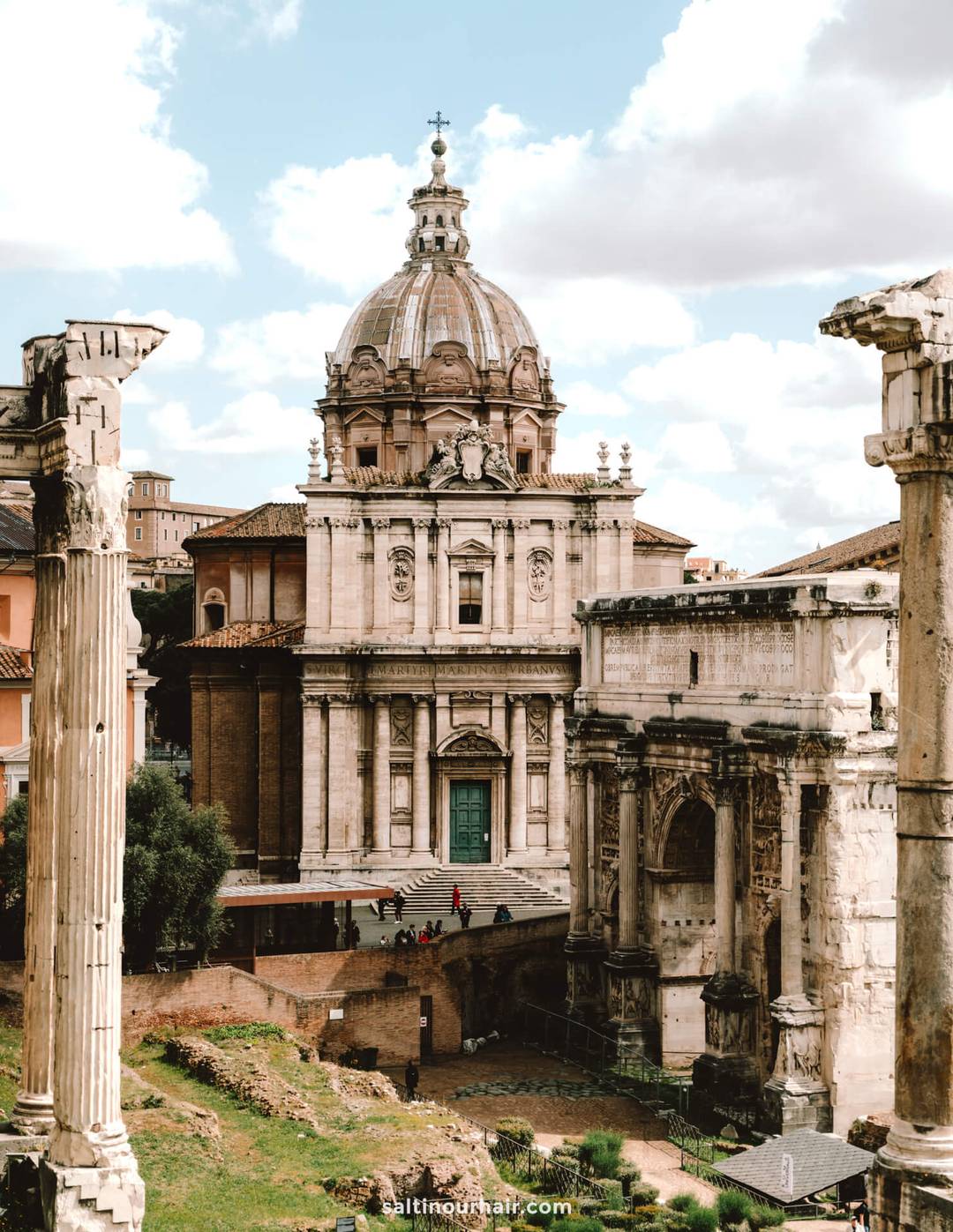 Ancient Roman ruins with tall columns in the foreground and an ornate Baroque church with a domed roof in the background&mdash;an iconic scene to include on your Italy 7 day itinerary under a partly cloudy sky.
