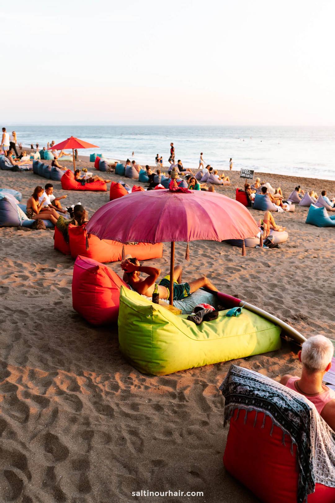 colorful bean bags on a beach with umbrellas and people enjoying the sunset in Canggu Bali 