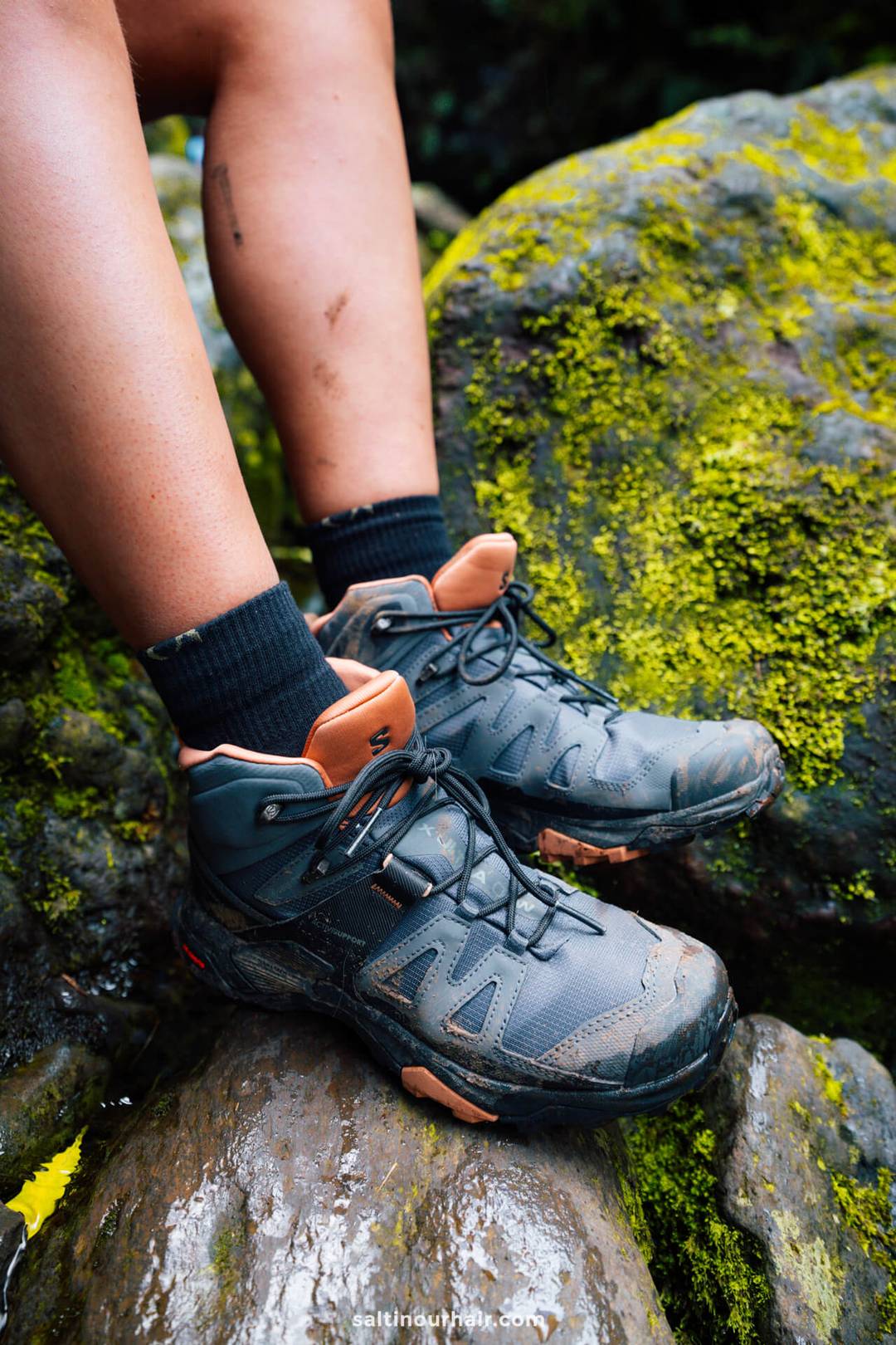 Iemand met zwarte wandelschoenen en zwarte sokken rust met de voeten op met mos bedekte rotsen, met benen die wat vuil en schrammen vertonen &mdash; misschien na het verkennen van ruige paden waarvoor wandelkosten op Madeira nodig waren.