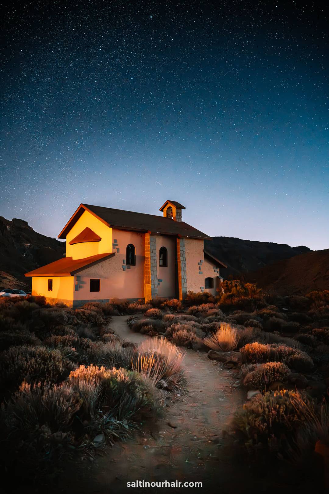 A small, illuminated church sits in a shrub-filled landscape beneath the clear, starry night sky of Teide National Park, Tenerife.