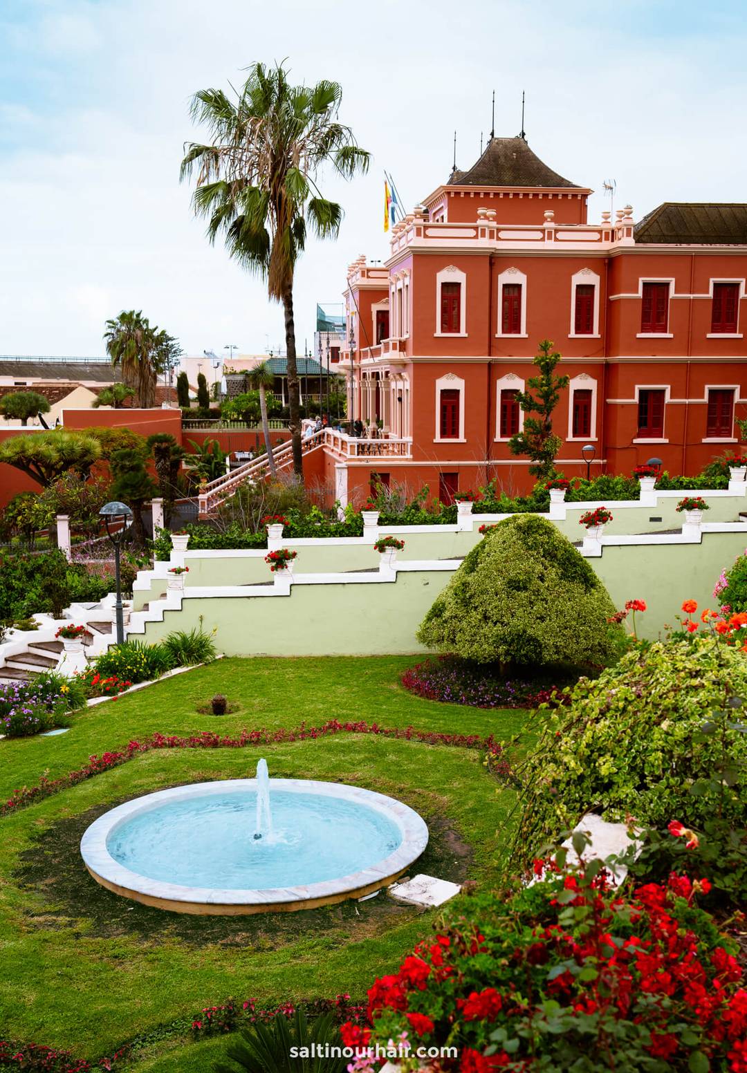 Marquesado de la Quinta Roja Garden with red Club Social Liceo Taoro building in the background under a partly cloudy sky&mdash;one of the charming things to do in La Orotava.