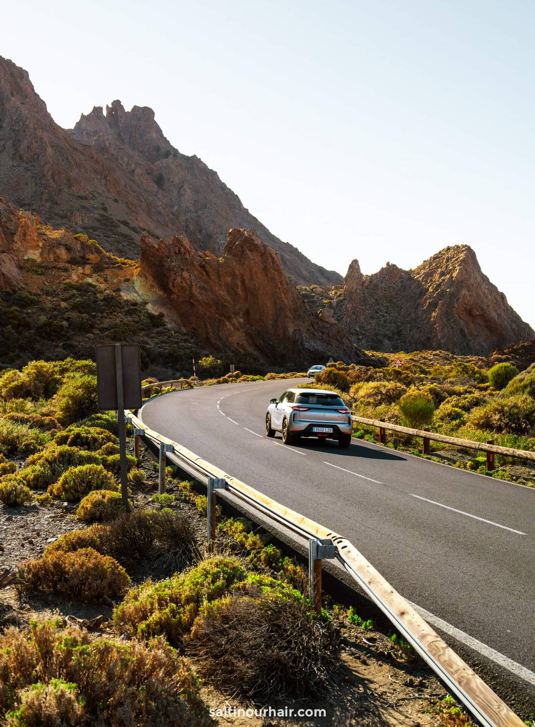 A car drives along a winding road through the mountainous, rocky landscape of Teide National Park
