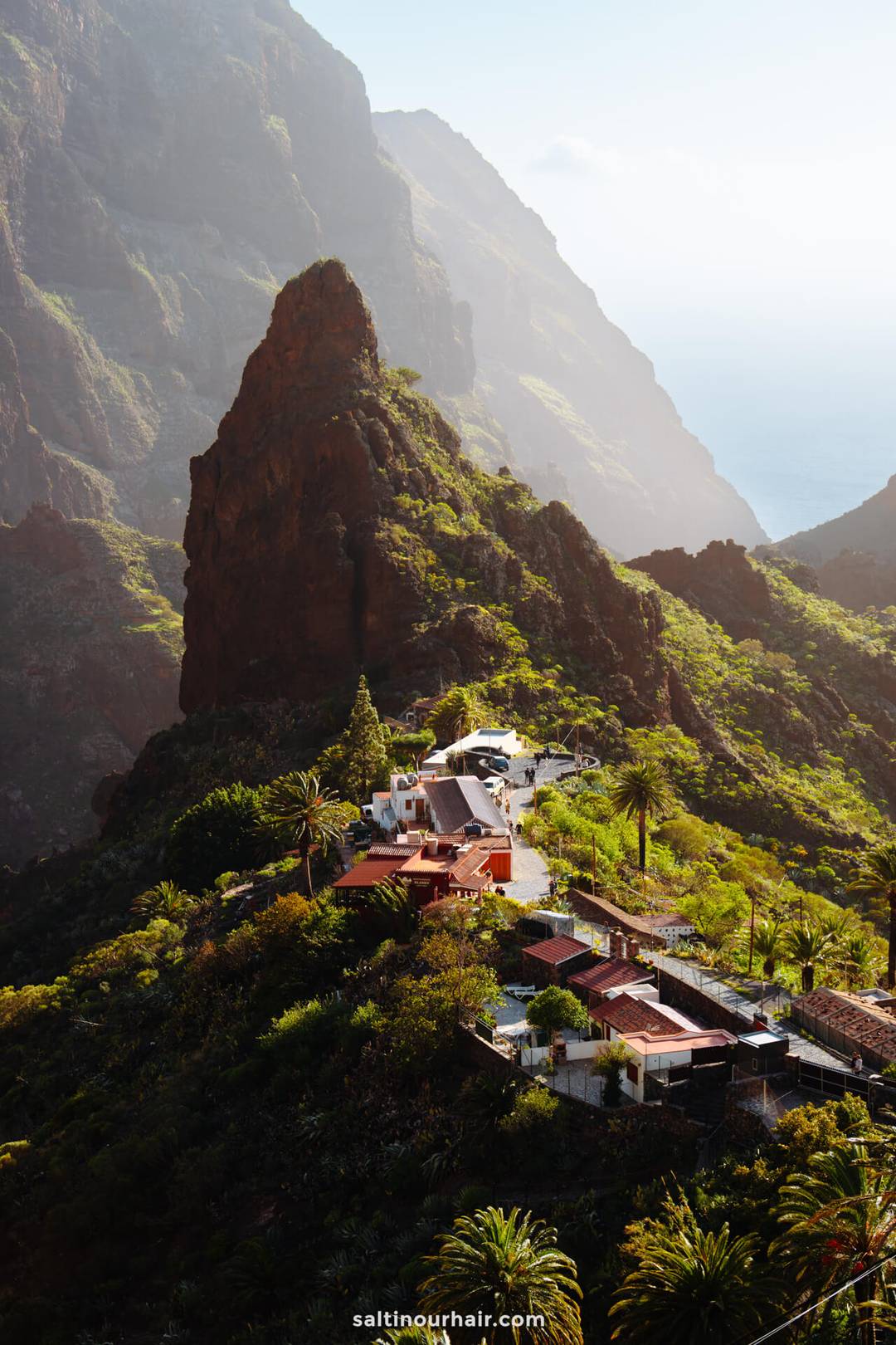 Charming small village with red-roofed houses nestled among lush green mountains, a rocky peak, and the ocean in the distance&mdash;Masca Tenerife offers breathtaking views and serene natural beauty.