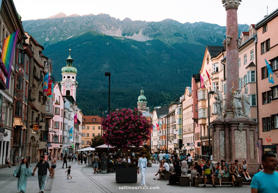 A bustling pedestrian street lined with colorful buildings and flags, where people stroll and relax, set against mountain views-a perfect spot to discover things to do in Innsbruck.