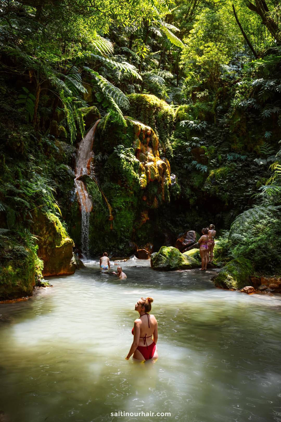 People swim and relax in a natural pool surrounded by lush greenery and a small waterfall in a forested area&mdash;one of the best things to do in S&atilde;o Miguel, Azores for nature lovers.