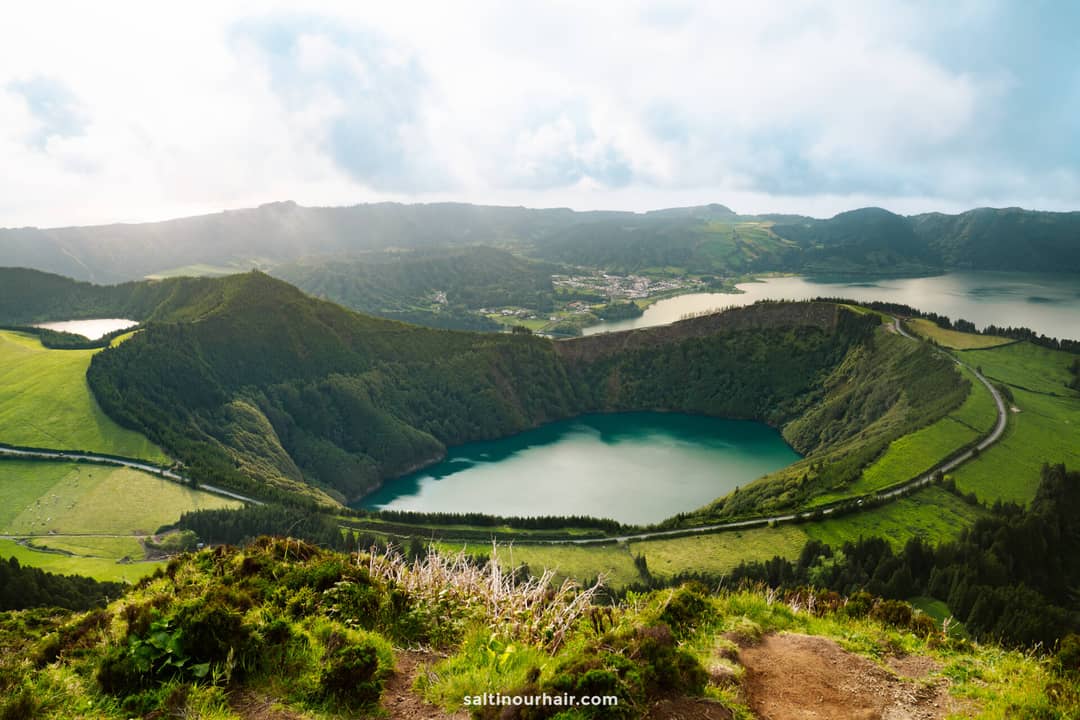 A wide view of Sete Cidades, a twin lake in a volcanic crater surrounded by green hills and a winding road&mdash;one of the must-see things to do in S&atilde;o Miguel, Azores, Portugal.