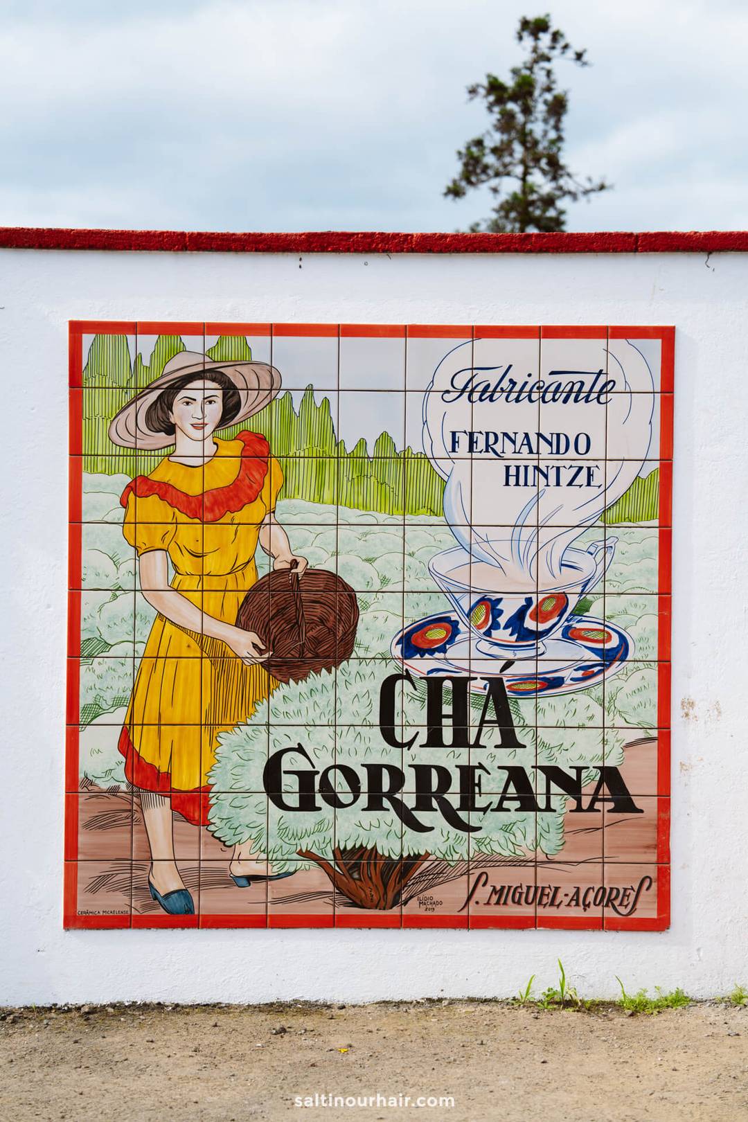 A colorful tile mural depicts a woman holding a basket, with text advertising F&aacute;brica de Ch&aacute; Gorreana and a tea set, set against a rural landscape&mdash;one of the unique things to do in S&atilde;o Miguel, Azores