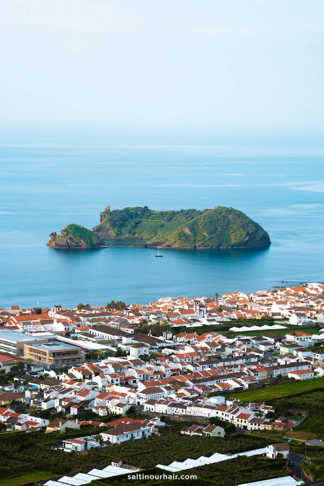 A small green island sits in the blue ocean near a coastal town of Vila Franca&nbsp;with white buildings and red roofs, offering a glimpse of the many things to do in S&atilde;o Miguel, Azores
