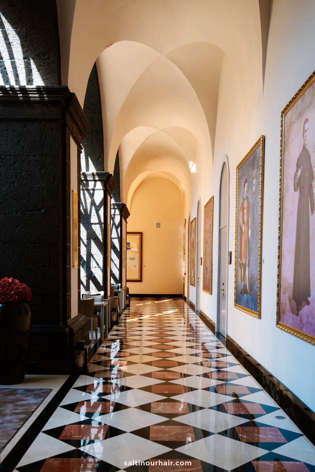 A hallway with arched ceilings, large portraits on the walls, geometric patterned floor tiles, and sunlight casting shadows through windows&mdash;capturing the charm you might find while exploring things to do in S&atilde;o Miguel.