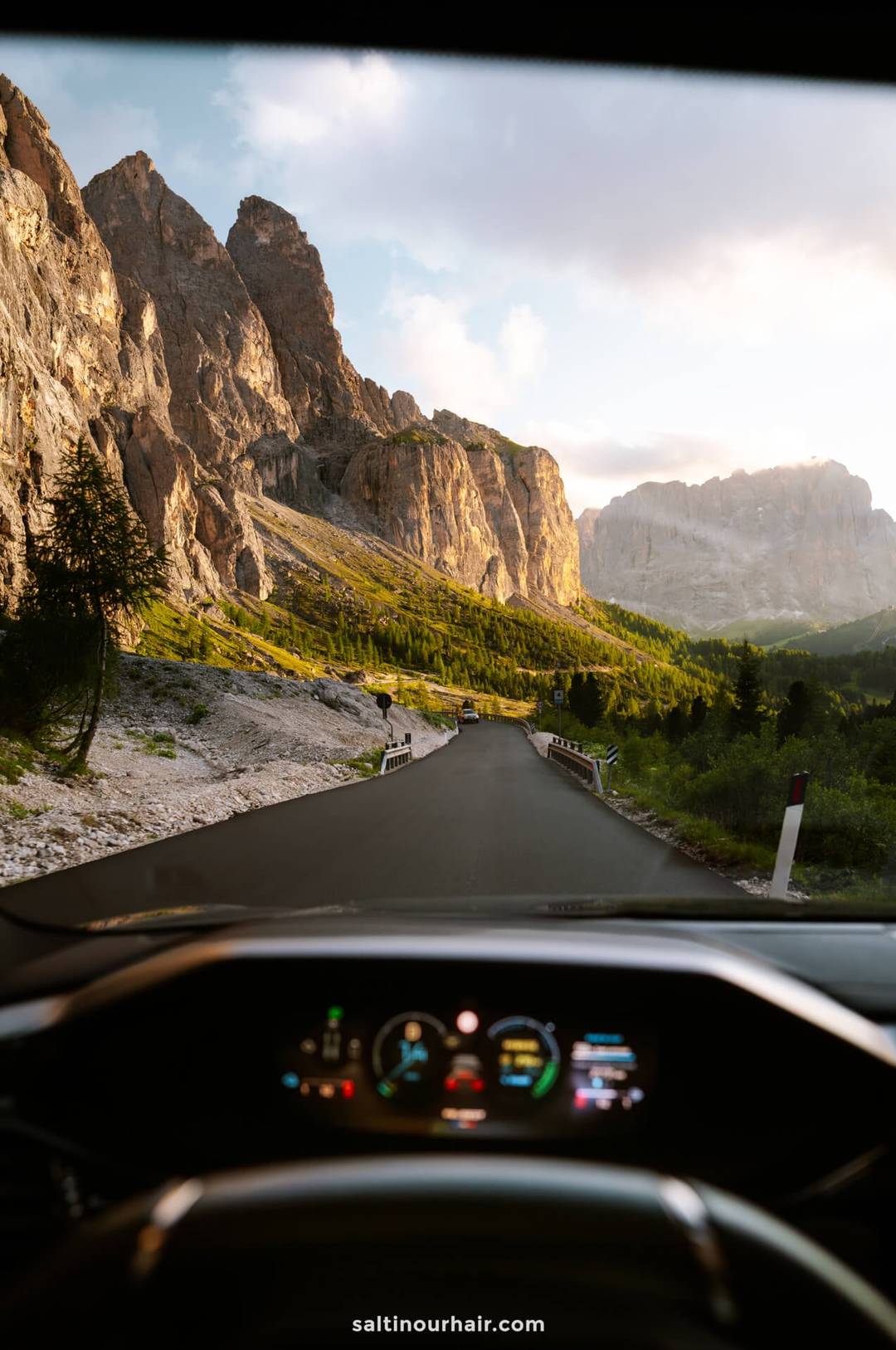 View from inside a car driving on a mountain road at sunset, with rocky cliffs and greenery on either side&mdash;an unforgettable experience of driving a car in Dolomites, Italy.