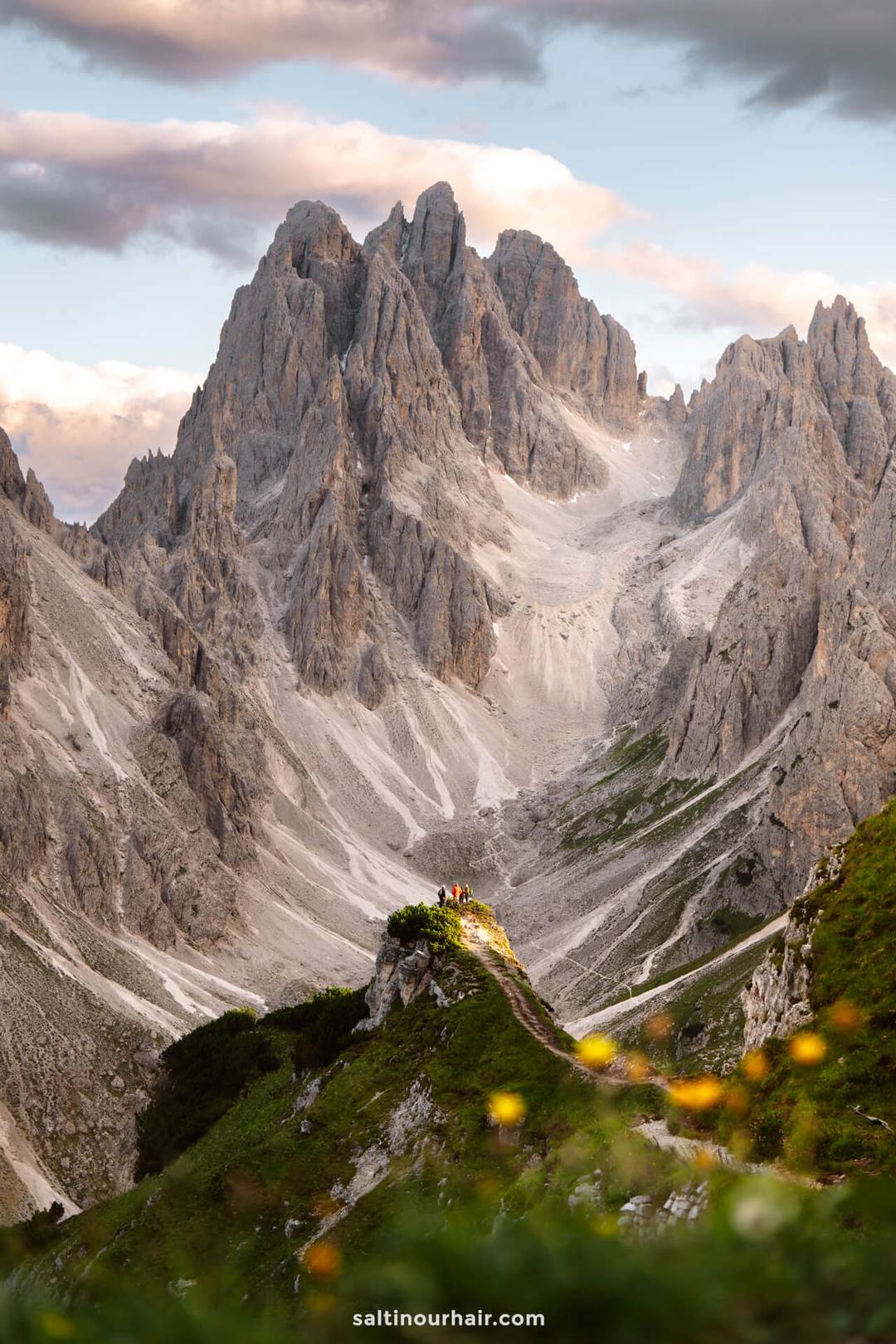 A group of people stands on a grassy ridge in the Dolomites, with dramatic rocky mountains in the background under a partly cloudy sky&mdash;Cadini di Misurina is one of the top things to do in the Dolomites for breathtaking views.