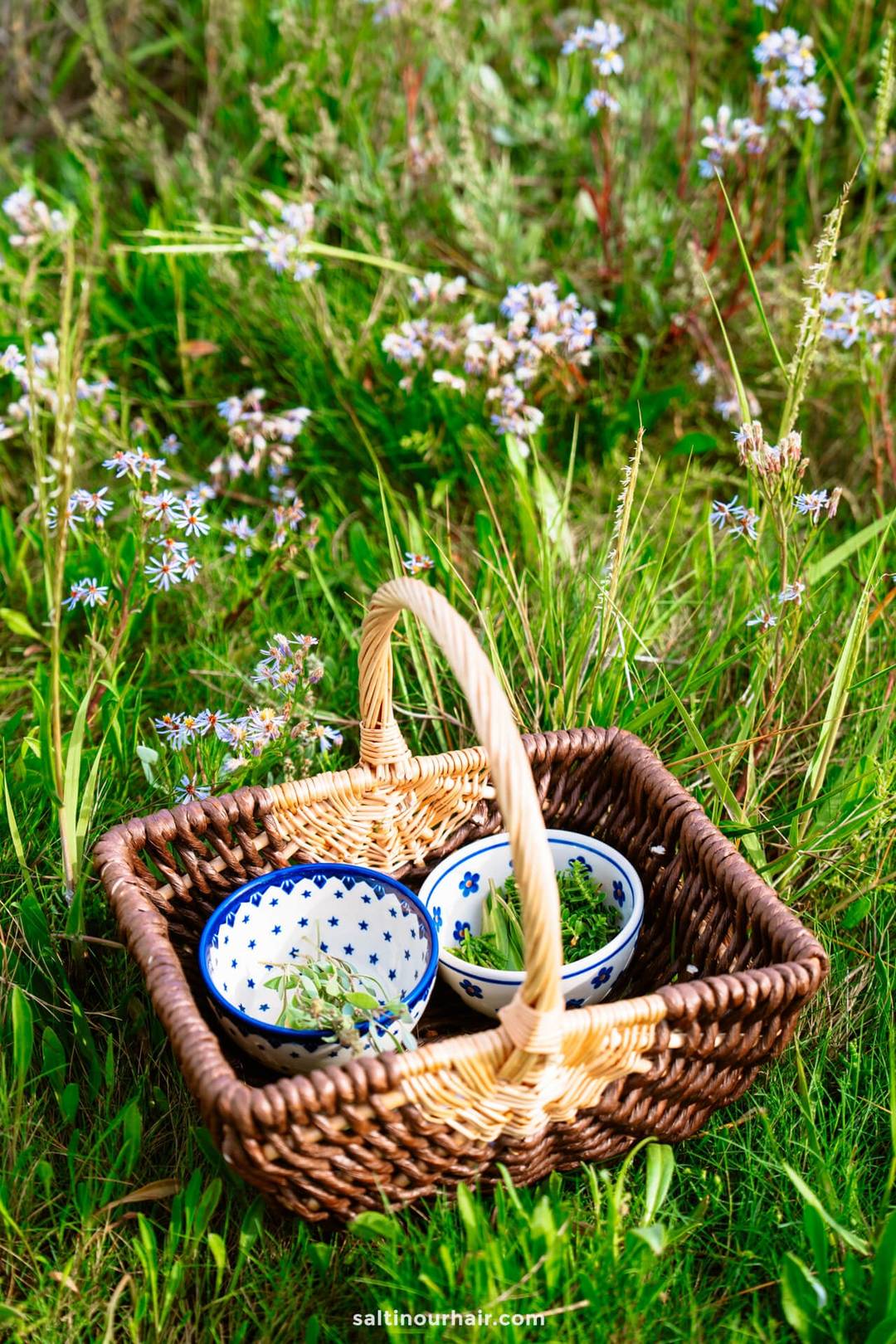 A wicker basket with three patterned bowls containing herbs, placed on grass surrounded by wildflowers&mdash;perfect inspiration for your Denmark itinerary.