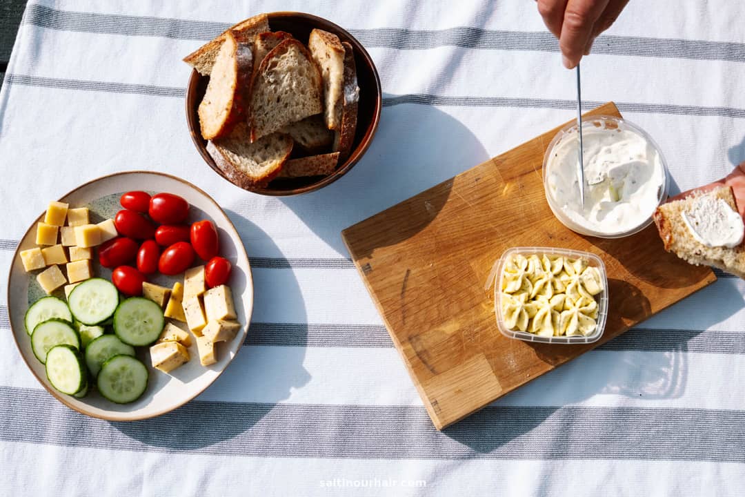 A plate with sliced cucumber, cheese cubes, and cherry tomatoes, a bowl of bread, and a board with cheese spread and chopped cheese on a striped tablecloth&mdash;perfect for planning your Denmark itinerary.