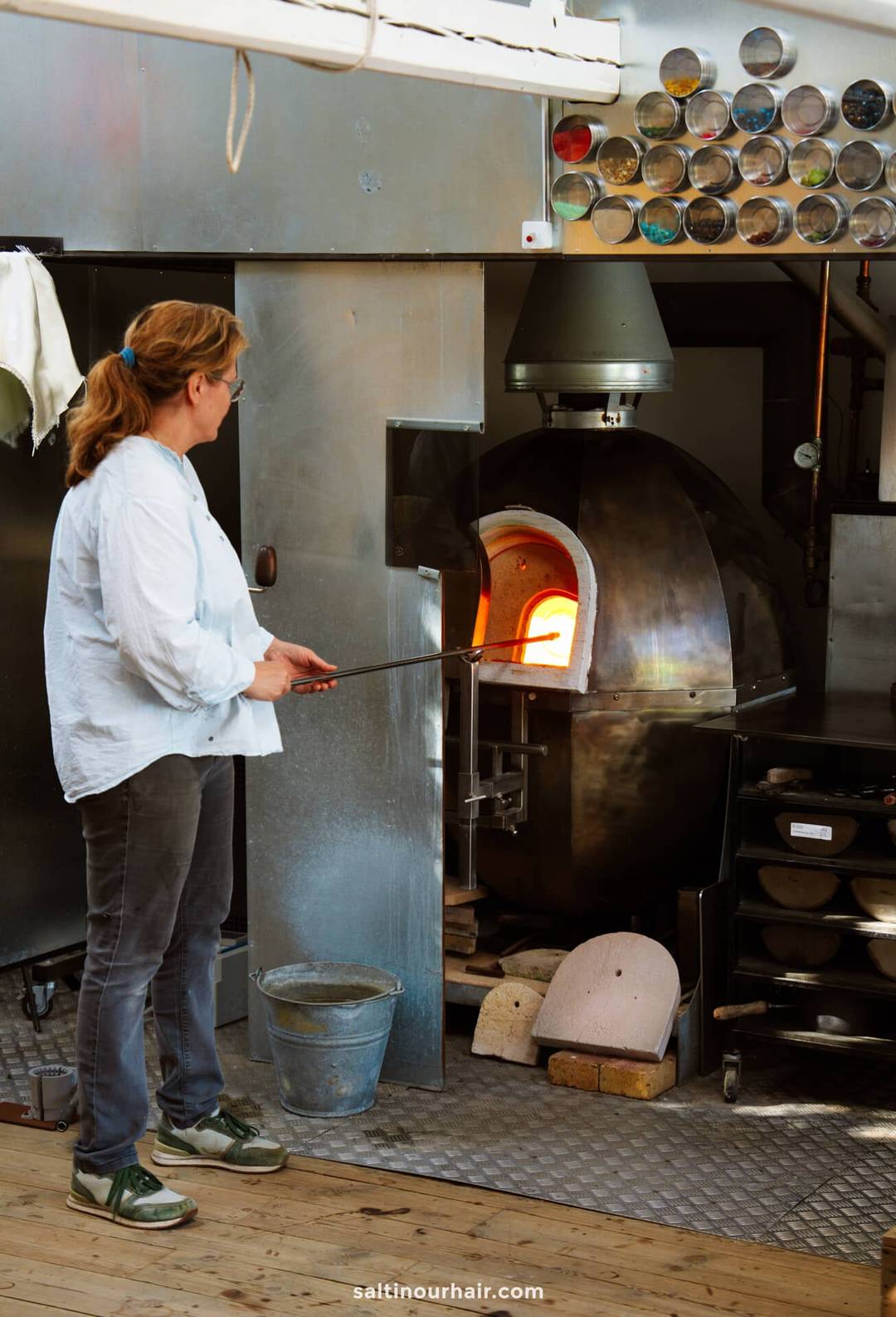 A person stands in front of a glassblowing furnace in Denmark, holding a metal rod with molten glass&mdash;an unforgettable experience to add to any Denmark itinerary.