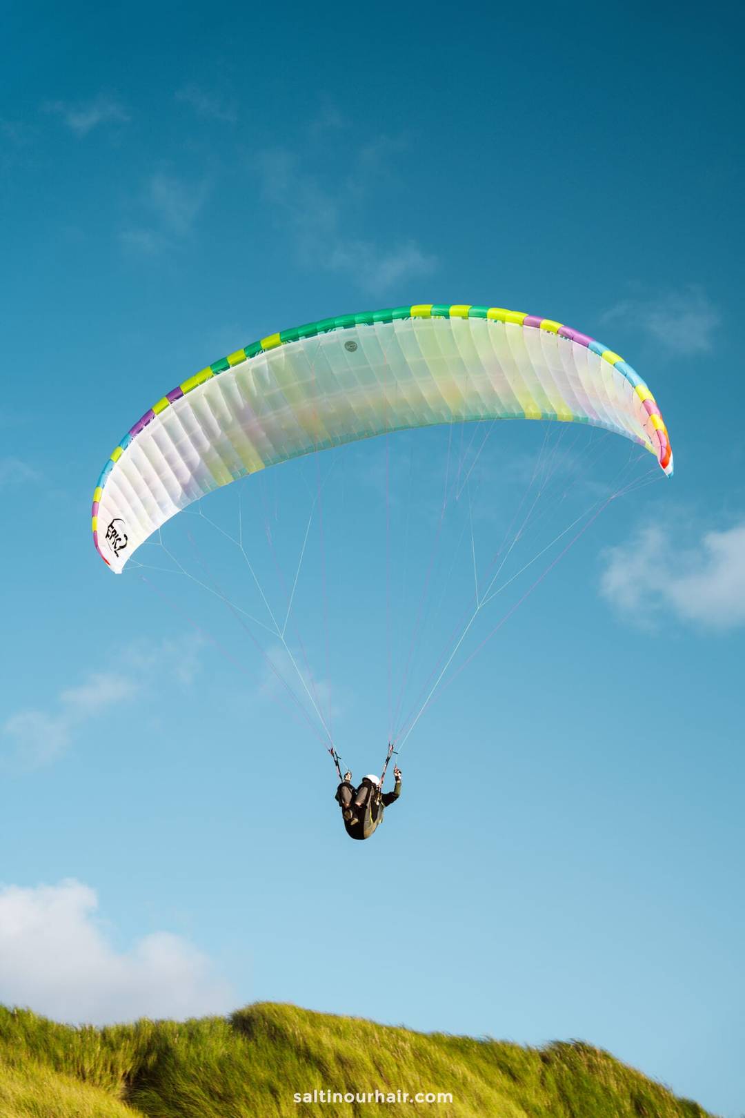 A person paraglides above grassy hills under a clear blue sky, capturing the adventurous spirit of any Denmark itinerary.