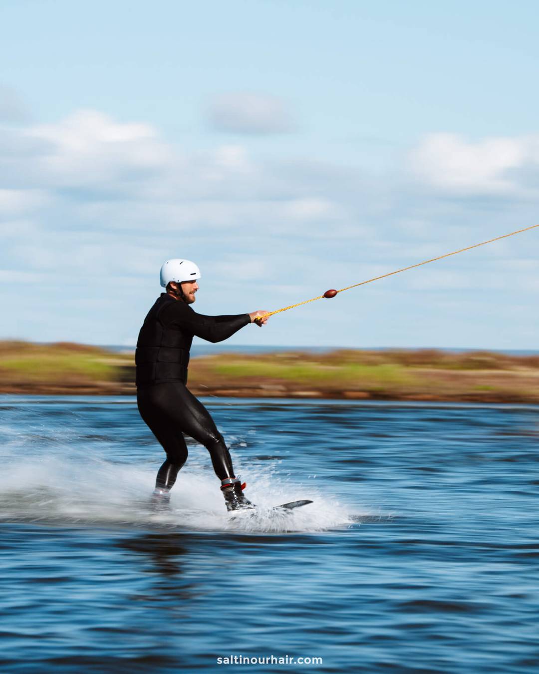 A person wearing a helmet and wetsuit is wakeboarding on a body of water, holding onto a tow rope&mdash;an exciting adventure to consider adding to your Denmark itinerary.