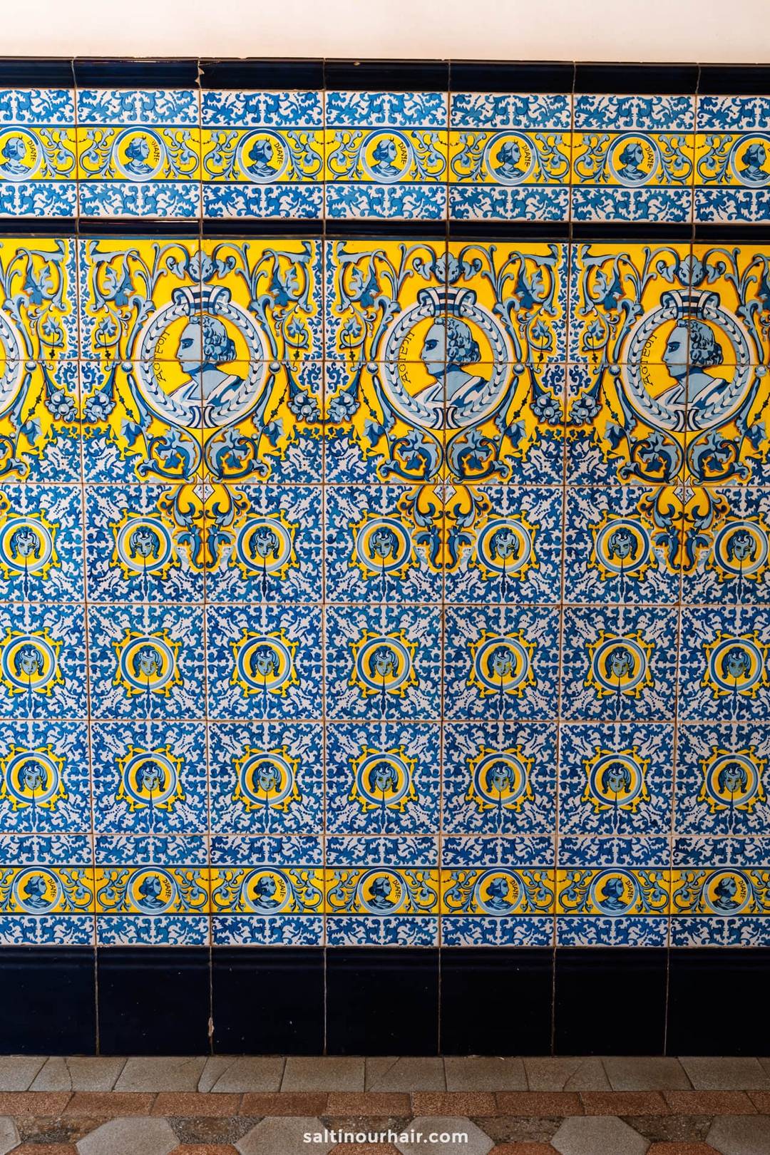 Een decoratieve muur van blauwe, gele en witte keramische tegels met ingewikkelde bloem- en geometrische ontwerpen, typerend voor de levendige stijl in San Crist&oacute;bal de La Laguna, Tenerife.
