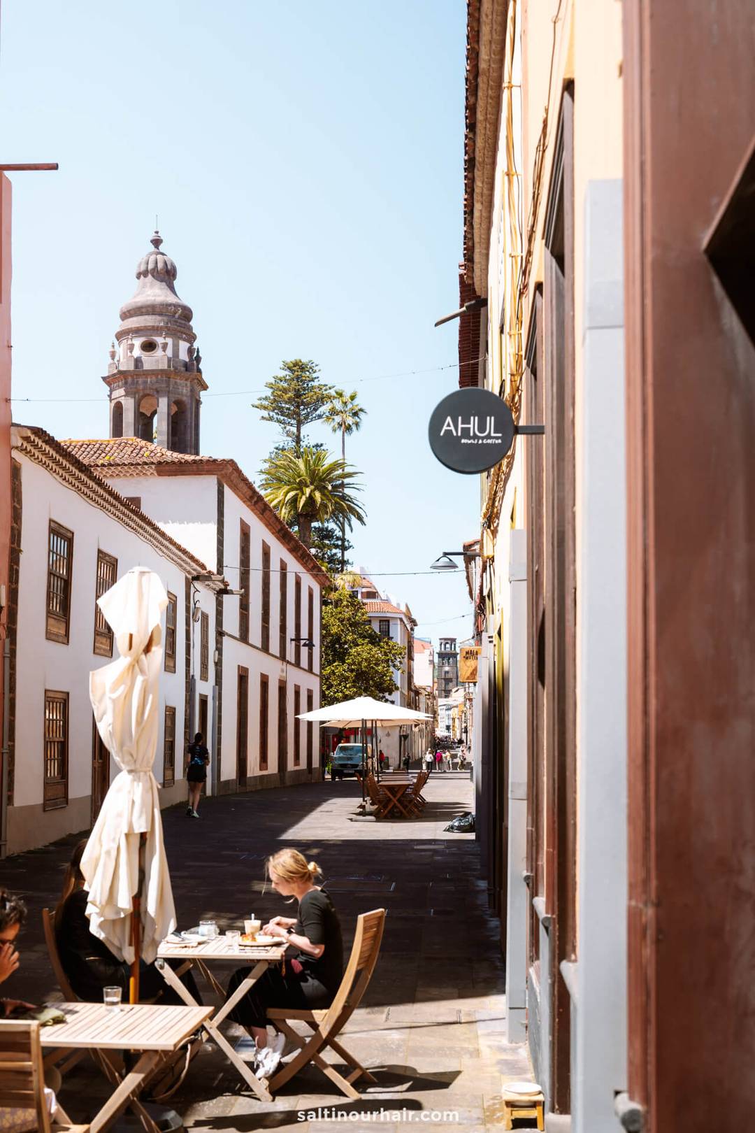 Een smalle straat in San Crist&oacute;bal de La Laguna, Tenerife, met een terras, dinerende mensen, witte gebouwen en de kathedraal van La Laguna op de achtergrond.