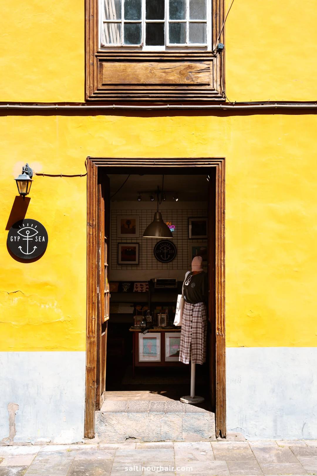 Open deuropening van een geel gebouw in San Crist&oacute;bal de La Laguna, Tenerife, toont het interieur van een kleine winkel met een etalagepop en diverse artikelen.