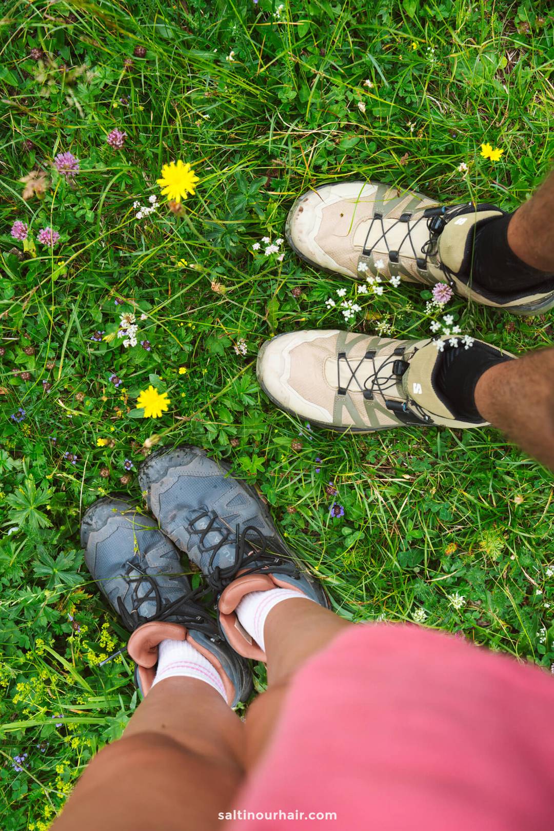 Two pairs of hiking shoes on green grass with scattered wildflowers, viewed from above&mdash;capturing a peaceful moment along the scenic Adolf Munkel trail.