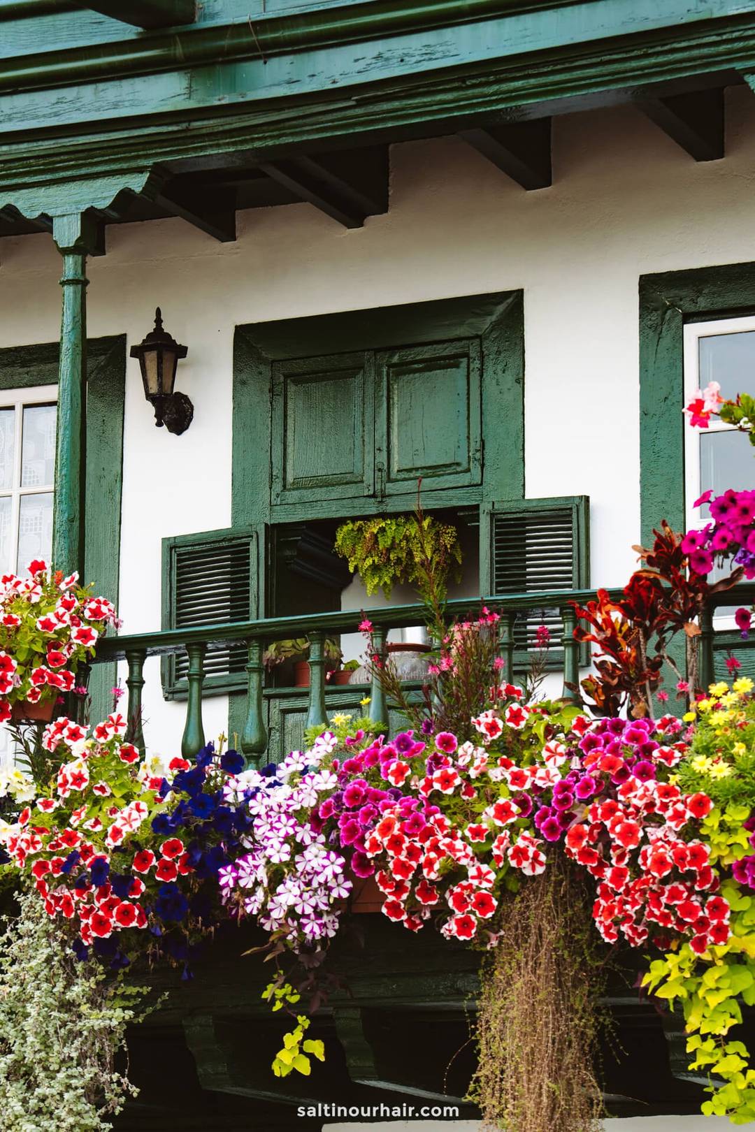 A green wooden balcony with a half-closed window, decorated with a variety of colorful flowers, attached to a white building&mdash;typical charm found in La Palma, Canary Islands.