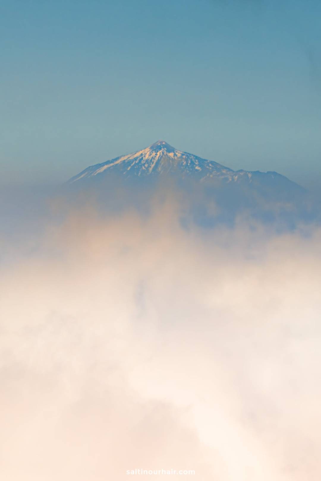 Snow-capped mountain peak rising above a layer of clouds under a clear blue sky&mdash;discover this breathtaking view on La Palma, the hidden gem of the Canary Islands.