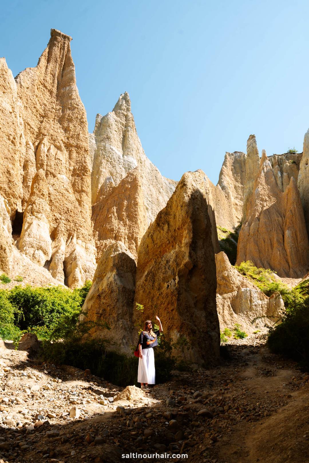 A person stands on rocky ground surrounded by tall, jagged limestone formations under a clear blue sky&mdash;a must-see stop on any New Zealand South Island itinerary.