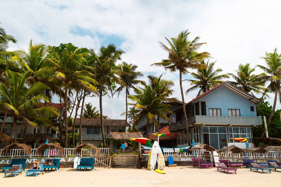 Kabalana Beach surf school in Ahangama, Sri Lanka, with surfboards, thatched loungers, and palm trees.