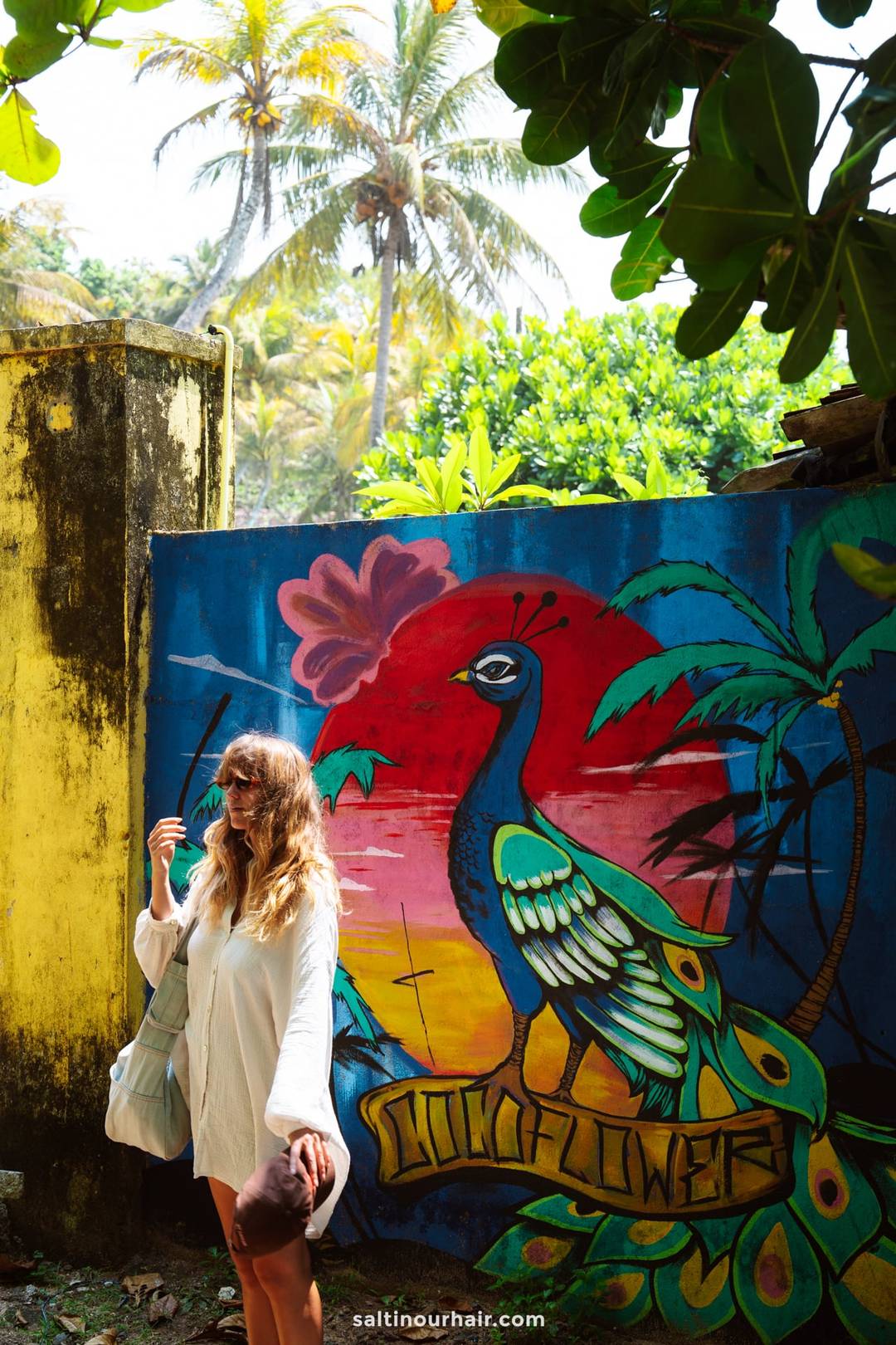 Woman in white dress standing beside the colorful Coconut Beach mural in Ahangama, Sri Lanka.