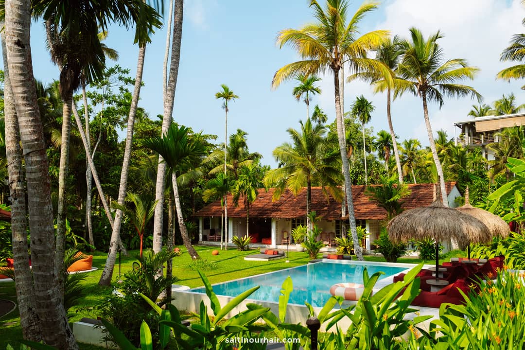 Tropical resort pool surrounded by tall palm trees and lush gardens with a red-tiled villa in Ahangama, Sri Lanka.