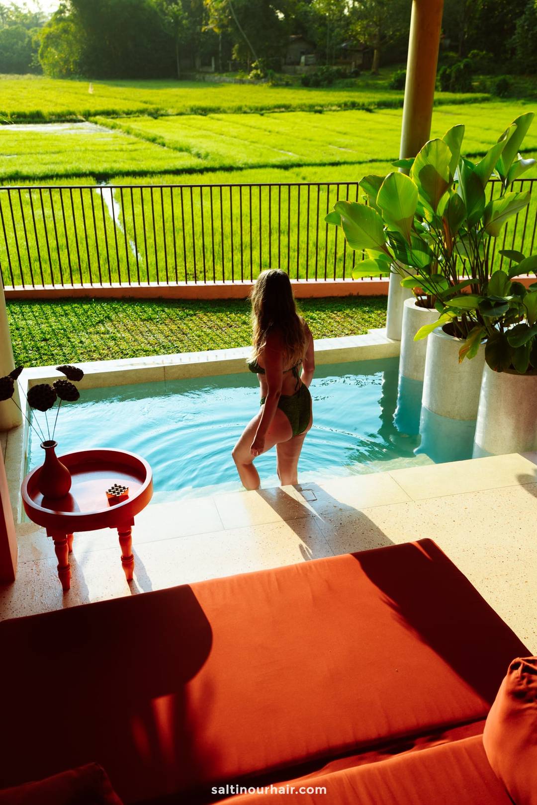 Woman in green bikini stepping into a private plunge pool overlooking lush rice paddy fields at a villa in Ahangama.