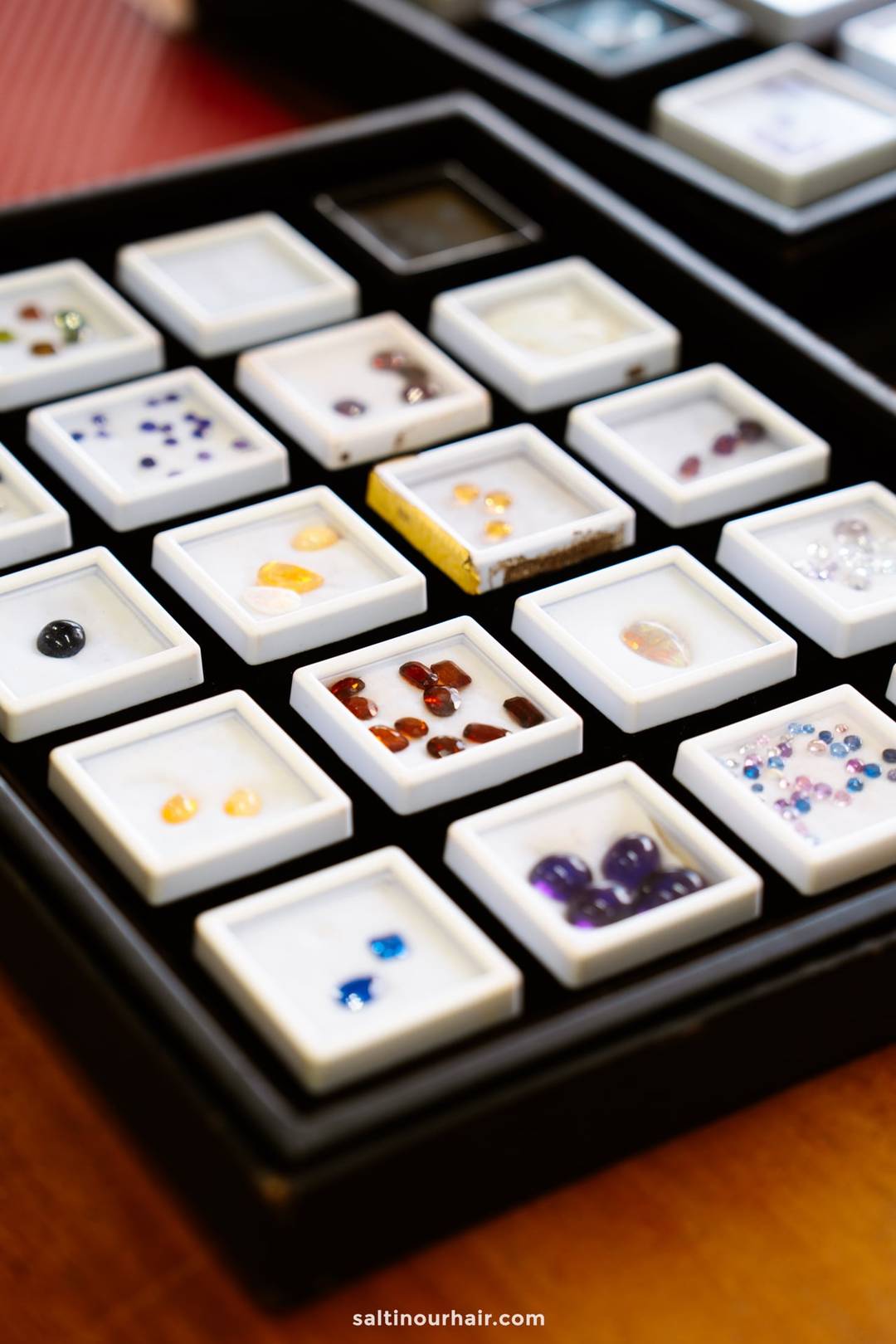 Collection of loose gemstones displayed in small white specimen boxes on a black tray at a jewelry shop in Ahangama.