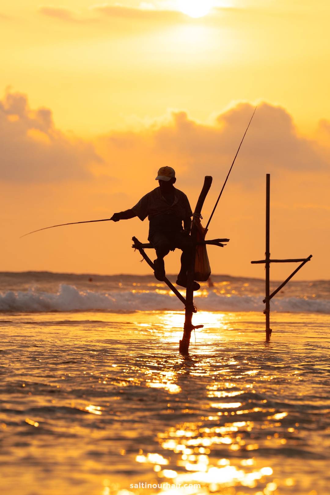 Traditional stilt fisherman perched on a cross-shaped pole casting a rod at golden sunset in Ahangama, Sri Lanka.