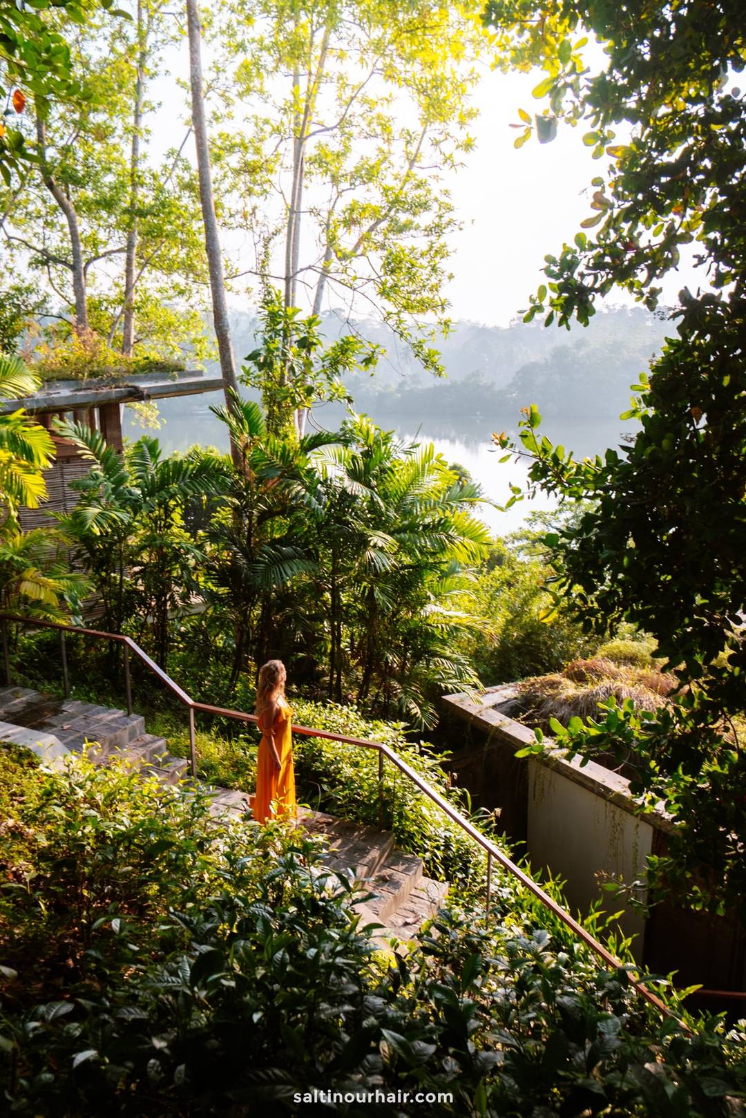 Woman in orange dress standing on stone steps overlooking misty Koggala Lake, Sri Lanka.