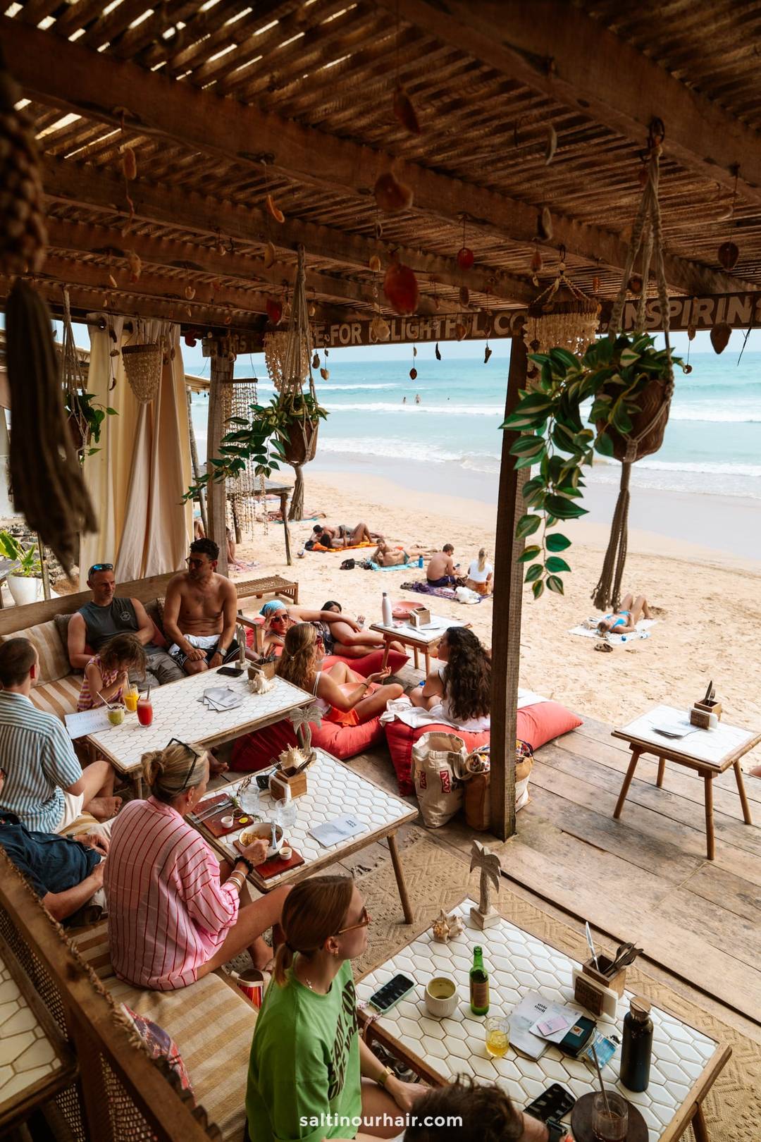 Beachfront caf&eacute; with rustic thatched roof, guests dining on floor cushions overlooking Ahangama Beach, Sri Lanka.