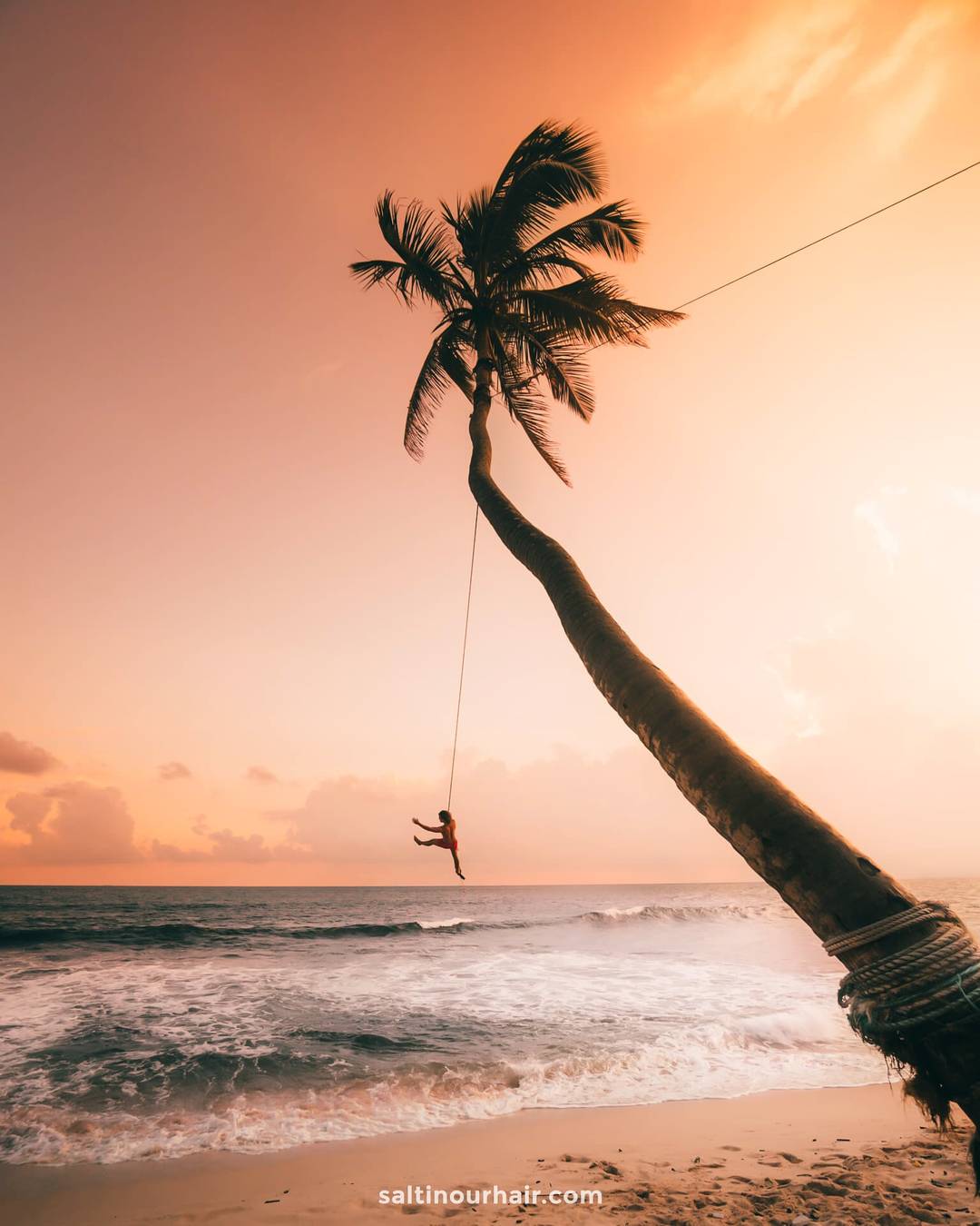 Person swinging on the Palm Swing rope at Dream Cabanas beach in Ahangama, Sri Lanka, at golden sunset.