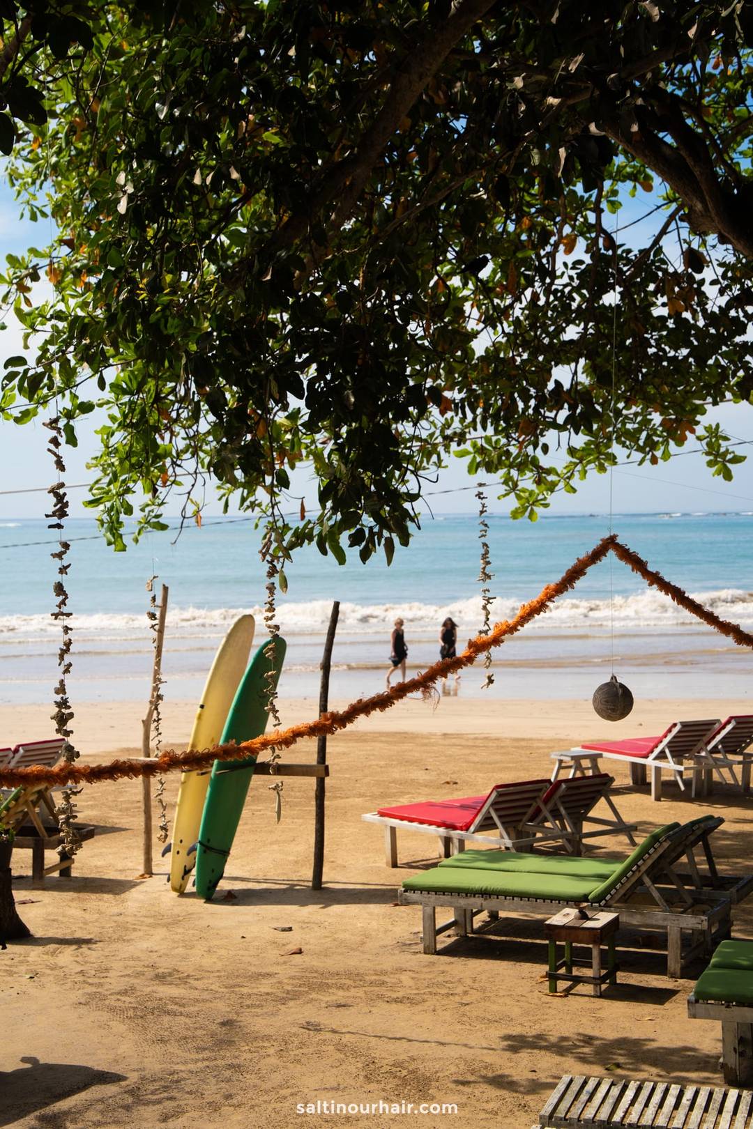 Kabalana Beach in Ahangama, Sri Lanka, with surfboards, colorful sun loungers, and two people strolling along the shore.