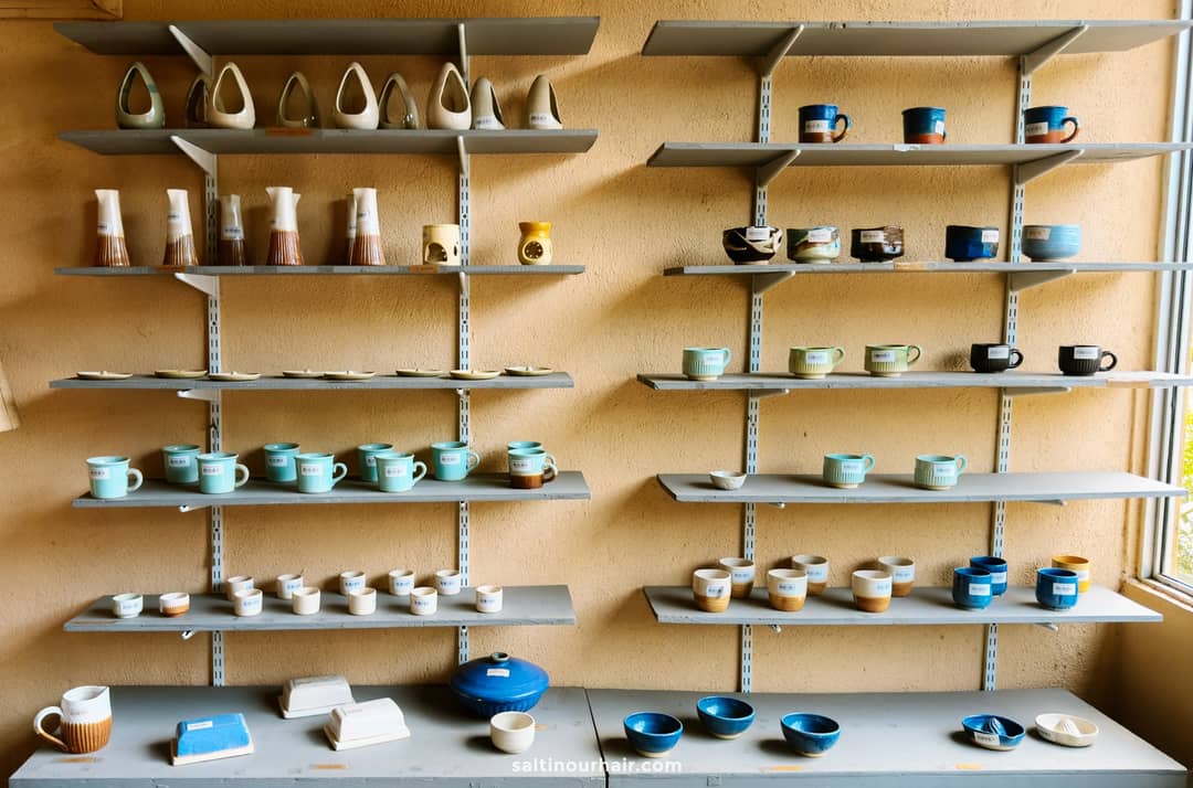Handmade ceramic mugs, bowls, and vases displayed on wall-mounted shelves at a pottery workshop in Ahangama.