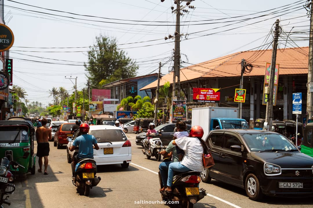 Busy main road traffic in Ahangama with tuk-tuks, scooters, and cars passing colorful roadside shops.