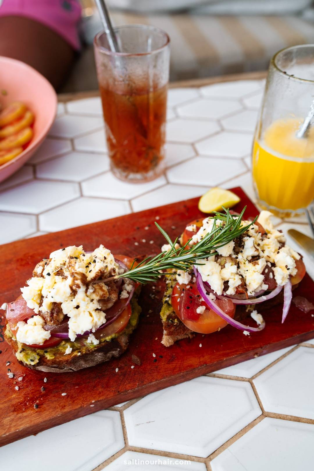 Two open-faced toasts topped with crumbled feta, tomato, and red onion on a wooden board in Ahangama, Sri Lanka.