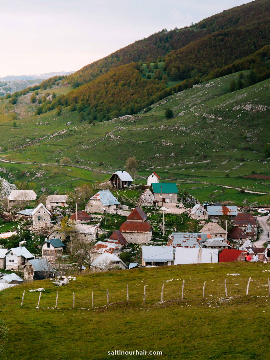 A small rural village with houses scattered on green hills, surrounded by trees and mountains under a cloudy sky&mdash;an ideal escape after exploring Sarajevo things to do.