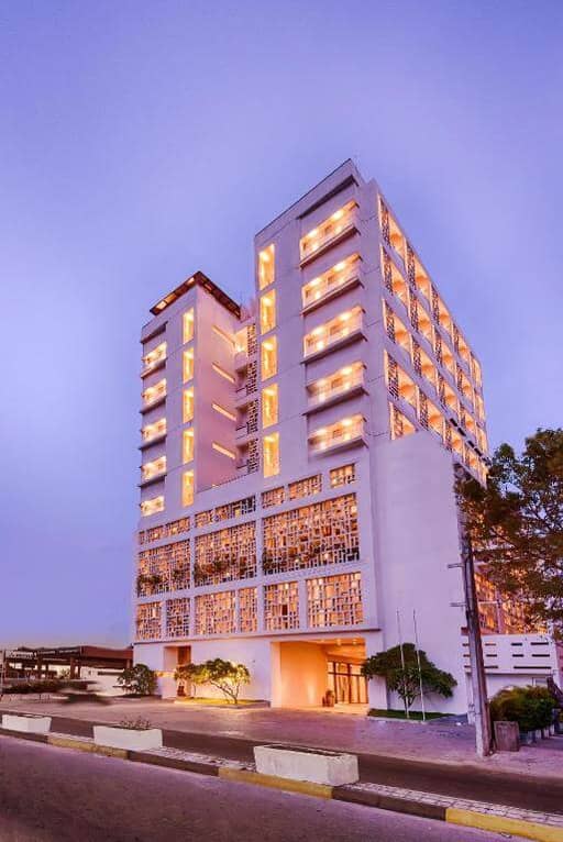 A modern multi-story hotel building, Jetwing Jaffna, features illuminated balconies and a geometric facade, pictured at dusk beneath a clear sky.